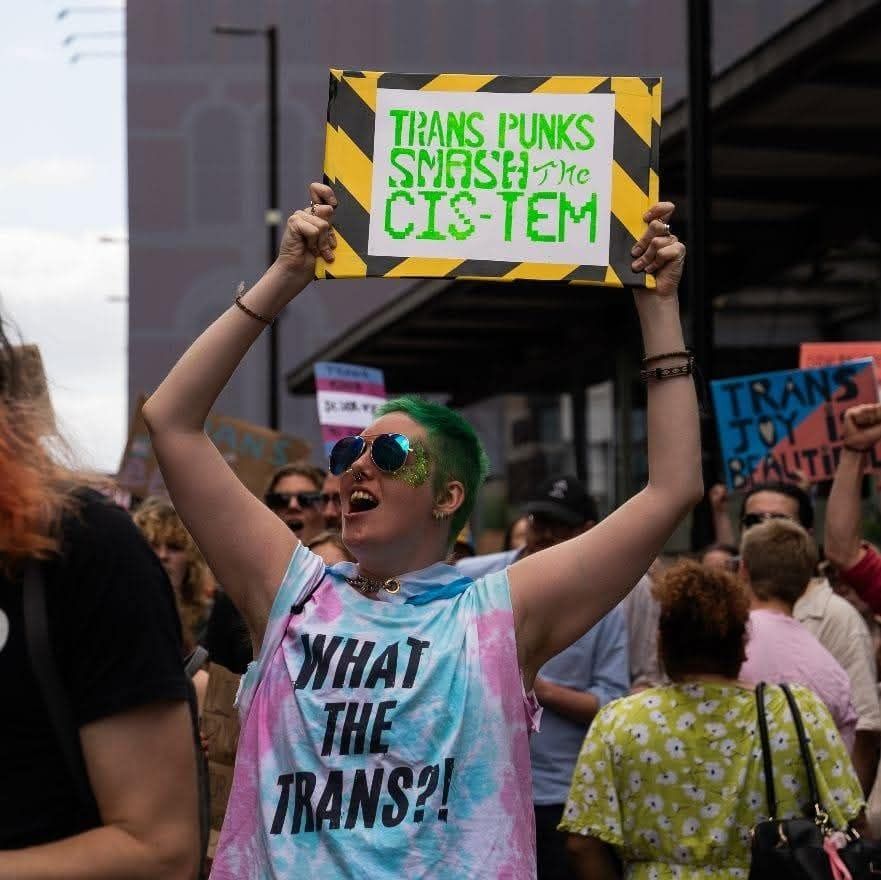 Gurge wearing a What The Trans top holding a sign saying TRANS PUNKS SMASH the CIS-TEM